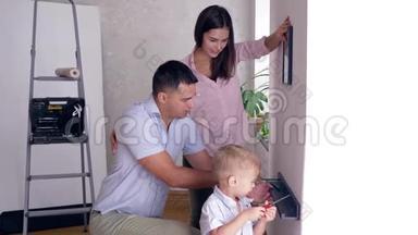 爸爸在公寓装修期间教儿子用螺丝刀把架子栓到墙上，妈妈在附近挂画